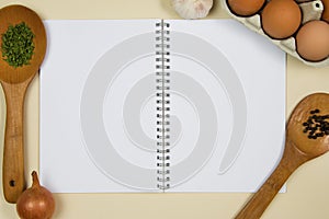 Wooden ladles on a dark wooden cutting boardWooden ladles with spices, eggs and garlic with a blank notebook page