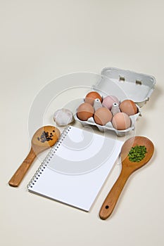 Wooden ladles with some herbs and food spicesm eggs and blank notebook