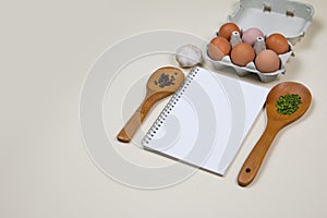 Wooden ladles with some herbs and food spicesm eggs and blank notebook