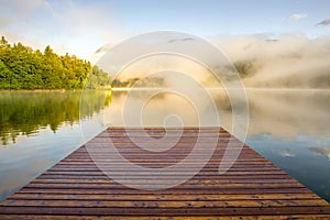 Wooden landing jetty at sunrise. Foggy morning at lake Bohinjsko, Slovenia.