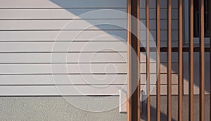 Wooden lath in front of white artificial wood and gray Sheetrock wall with part of glass window frame