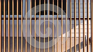 Wooden lath in vertical pattern in front of glass windows with white artificial wood and gray sheetrock background