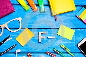 A wooden letter of grade F minus the student`s desk. School supplies on a blue wooden table. The concept of higher school