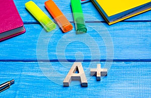 Wooden letter A plus on the student`s desk. School supplies on a blue wooden table. The concept of higher school assessment, good