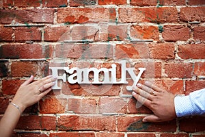 Wooden lettering family for valentine`s day and merry christmas on a background of a red brick wall held by a male and female han