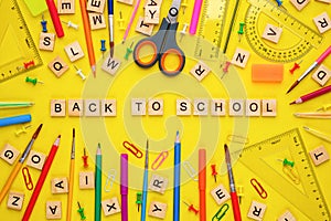 Wooden letters arranged in phrase back to school and office supplies on yellow background