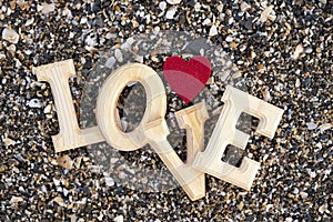 Wooden letters forming the word love with a red heart on a background of beach sand. concept of san valentine