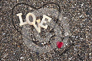 Wooden letters forming the word love with a red heart on a background of beach sand, inside a heart made with the fingers. concept