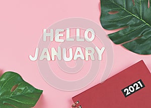 Wooden letters HELLO JANUARY  with  red 2021 diary or planner and monstera leaves on pink background . greeting new month and new