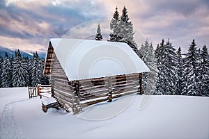 Wooden log cabin hut in snowy mountains under cloudy sky