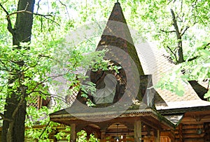 A wooden log hut with a patterned porch among green trees in the forest. An old log house among the trees. A porch with