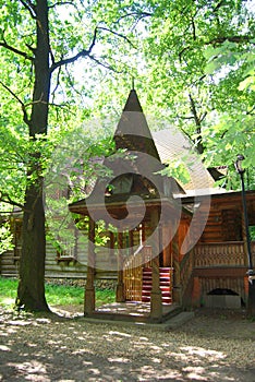 A wooden log hut with a patterned porch among green trees in the forest. An old log house among the trees. A porch with