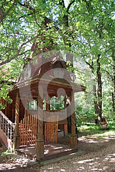 A wooden log hut with a patterned porch among green trees in the forest. An old log house among the trees. A porch with