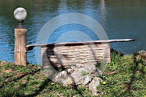 Wooden log used as improvised bench in shade of tree next to round white outdoor light mounted on tree stump and large rock on