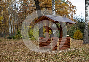 Wooden log well in retro style in autumn woods. Fetching water in the village with a bucket and rope.