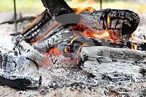 Wooden logs or firewood burn with red yellow flame among pieces of embers and live coals.