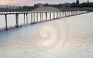 Wooden long bridge over a sea plait, river at sunset in perpektive, against a background of reeds, landscape