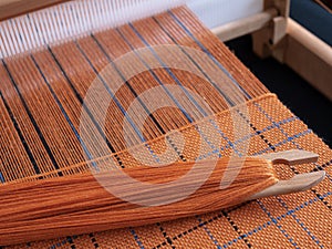 Wooden loom with shuttle and woven orange textile with striped pattern