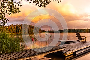 Wooden lounge chairs at Sunset on a pier on the shores of the calm Saimaa lake in Finland under a nordic sky with a rainbow