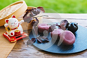 Wooden lucky cat figurine beside a plate of food on a table. Mochi asian dessert