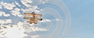 Wooden, made of plywood, small toy light aircraft biplane with propeller, flying in cloudy sky.