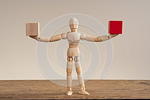 Wooden man extended his arms in different directions, hold two cubes, red and white.