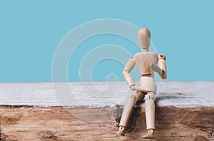 Wooden man mannequin sits on blue background.