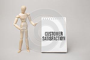 Wooden man shows with a hand text Customer Satisfaction concept on the notepad