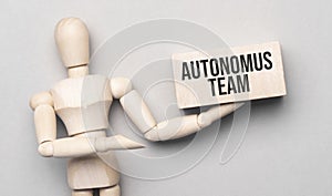 Wooden man shows with a hand to white board with text autonomus team, concept photo