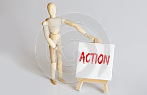 Wooden man shows with a hand to white easel with text ACTION