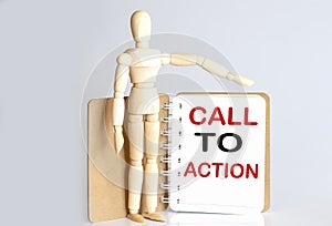 Wooden man shows with a hand to white notepad with text CALL TO ACTION