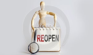 Wooden man shows with a hand to white notepad with text REOPEN