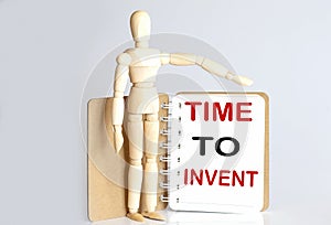 Wooden man shows with a hand to white notepad with text time to invent