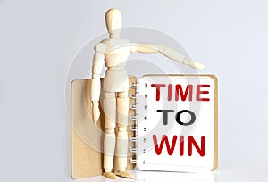Wooden man shows with a hand to white notepad with text time to win