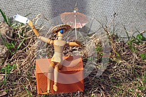A wooden man sits on a brick under an umbrella after the quarantine is lifted. He threw off his mask and began to