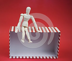 Wooden man sitting on empty gift box on red background