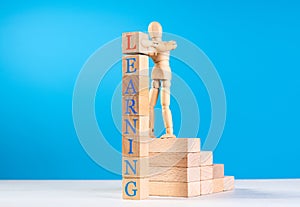 Wooden man stand on stairs of wooden bricks and put on last cube with red letter on top of tower.