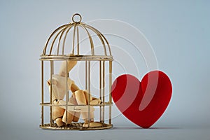 Wooden mannequin in a bird cage and free heart - Love and freedom concept