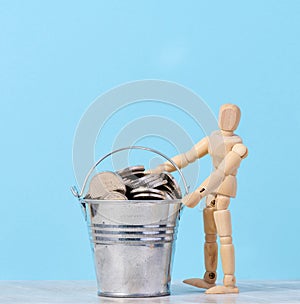 A wooden mannequin and coins in a miniature bucket on a blue background, a concept of high income, subsidy