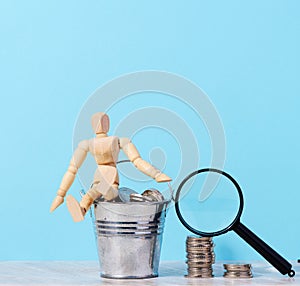 A wooden mannequin and coins in a miniature bucket on a blue background, a concept of high income, subsidy