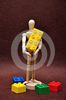 A wooden mannequin holding a building blocks with some smaller ones