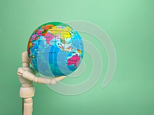 Wooden mannequin holding earth globe on a green background