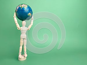 Wooden mannequin holding earth globe on a green background