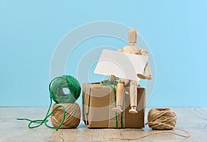 Wooden mannequin holding a white paper business card and gifts wrapped in brown craft paper on a blue background