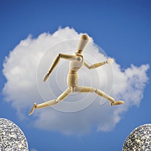 Wooden mannequin is jumping over the abyss at cloudy sky background
