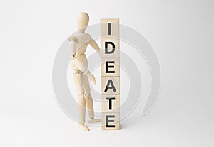 Wooden mannequin near tower of cubes with word ideate on table against light background photo