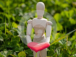 Wooden mannequin with a red heart on his hands in the grass. Concept of romanticism and love