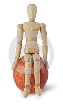 The wooden mannequin sits on a ripe apple