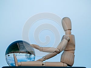 Wooden mannequin sitting with a crystal ball in his hands reflecting a landscape Ecology concept