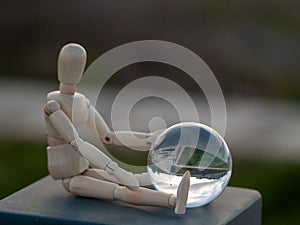 Wooden mannequin sitting with a crystal ball in his hands reflecting a landscape Ecology concept